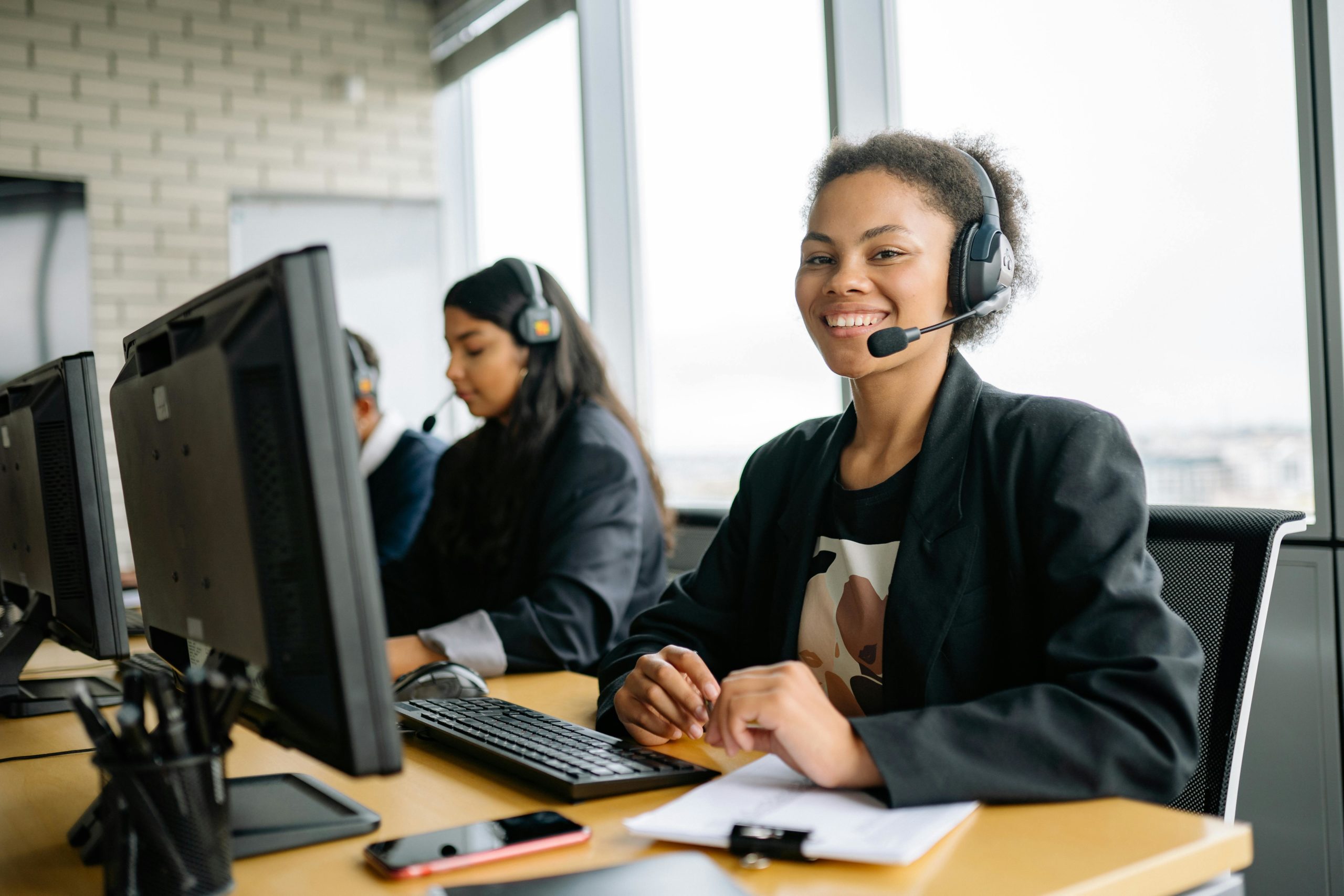 Smiling customer service representatives with headsets working in a bright modern office.
